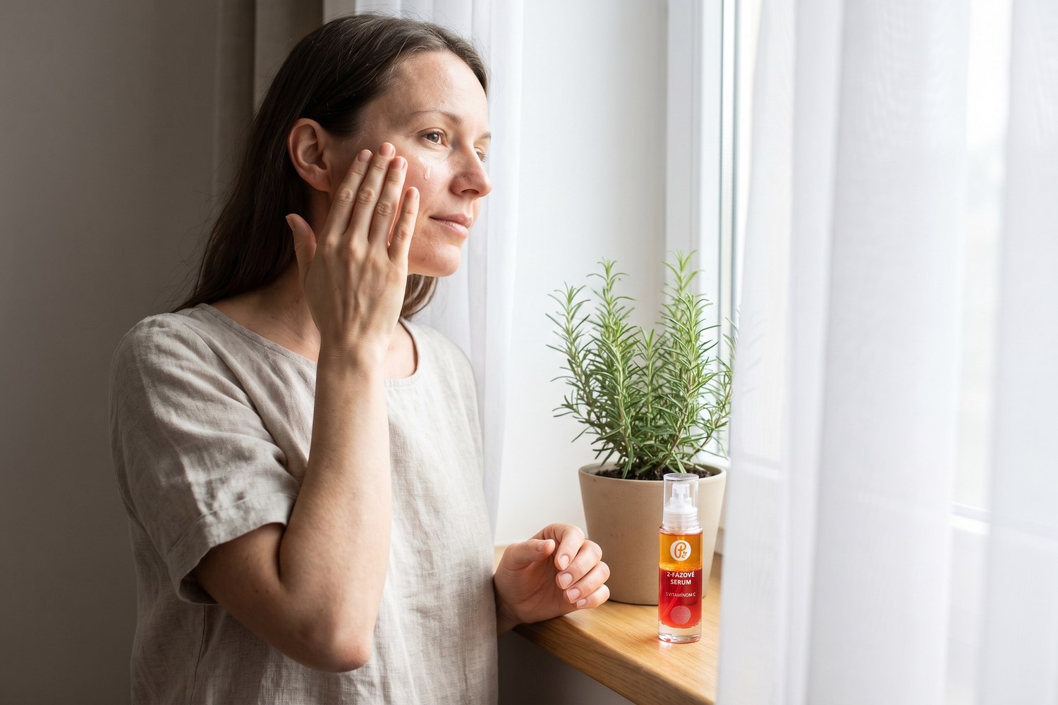 Žena si jemne nanáša rozjasňujúce sérum na tvár pred zrkadlom